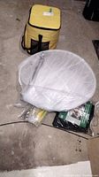 White mosquito tent mesh and large insect screen in plastic packaging on basement floor with cooler bag nearby