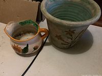 Pitcher and planter side by side on a table, visible sunflower and floral designs, size notes on tape inside pitcher