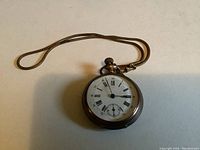 Gold-toned pocket watch with white face showing Roman numerals, attached to matching fob chain.
