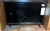 Front view of the 14 inch Insignia flat screen TV on wooden surface with remote in front.