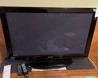 Front view of Samsung 42 inch plasma TV on stand with two remotes in front and power cord partially visible.