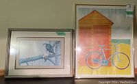 Two framed prints side by side; colorful bicycle and beach hut print on right, monochrome bird print on left.