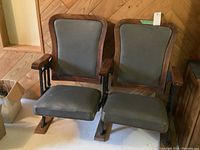 Pair of vintage cinema chairs with wood framed vinyl seats and solid cast base sitting next to each other on wood floor, showing the front and side views