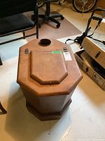 Side view of vintage wooden commode with top ventilation hole and removable lid in a basement setting.