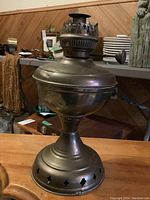 Front and side views of the vintage kerosene lamp showing brass tone metalwork, vent holes in base, and wick adjustment knob.