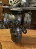 Front and side views of vintage brass kerosene lantern showing cylindrical base, glass lenses, and vented top with embossed design.