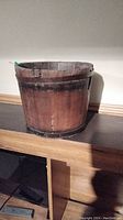 Full view of the vintage wooden bucket showing its round shape and aged wood finish with metal straps.