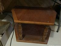 Wood side table featuring a rectangular top, turned legs, and a lower shelf. Medium brown wood finish. Shows some wear.
