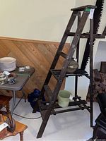 Front angle view of the vintage wooden ladder with slat shelves in a room with wood paneling and various items nearby.
