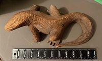 Wooden lizard sculpture placed next to a measuring tape showing length around 12 inches.