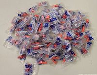 Over 100 pairs of individually packaged orange foam ear plugs scattered on a surface.