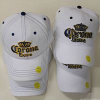 Four white Corona Extra baseball hats stacked in two pairs showing embroidered logos and yellow price stickers.