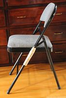 Side view of a single folding chair showing black metal frame and grey padded seat and backrest.