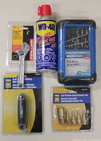 Front view of all five items in lot showing WD-40 can, wrench, drill bit set, hex key set, and quick coupler set