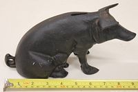 Side view of the black cast iron piggy bank measuring approximately 9 inches in length alongside a measuring tape.
