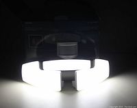 White solar motion activated security light powered on, showing bright white LED light panels arranged in a circular pattern about a central sensor.