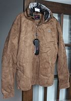 Front view of new brown men's jacket with tag hanging from zipper, suede-like material and faux fur lining at collar.