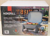 Box front showing the NexGrill Fortress 1-Burner Cast Aluminum Table Top Gas Grill with a visual of the grill and food cooking on grill surface.