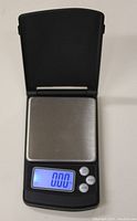 Opened Spectrum mini digital scale displaying zero on the blue backlit LCD. Stainless steel weighing platform visible.