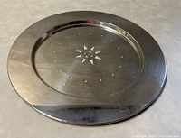 Top view of the round stainless steel serving tray highlighting the central star pattern and circular cutouts with a wide polished rim.
