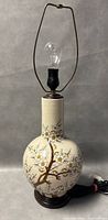 Full view of porcelain table lamp with floral crackle glaze, wood base, bulb and harp frame