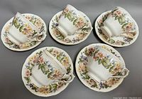 Five bone china teacups with matching saucers arranged on a gray surface showing floral pattern and gold trim.