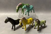 Frontal and side view of all five miniature horse figurines together showing varied colors and minor wear.