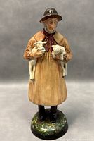Front view of the Royal Doulton figurine showing the figure holding two lambs, standing on a painted base.