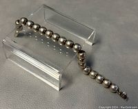 Photograph showing the entire 8 inch 925 sterling silver beaded bracelet laid on a textured gray surface with the bracelet displayed on an acrylic stand.