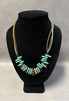 Front view of the beaded necklace on a black bust showing turquoise and amber beads with multi-strand design.