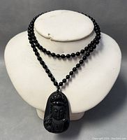 Front view of black beaded necklace displayed on white bust with carved obsidian Kuan Yin pendant