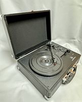 Open portable turntable showing platter, tonearm with needle, control knobs, and speaker grille inside.