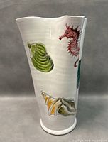 Side view showing the detailed painted seashells and red seahorse design on white pottery vase with scalloped top edge.