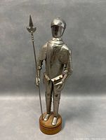 Front view of vintage knight statue in shining armour holding pole weapon on wooden base