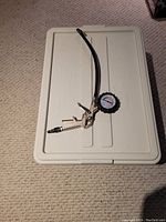 Manual tire inflator gun with pressure gauge placed on a beige plastic surface.