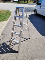 Front angle view of the 5-foot aluminum step ladder on pavement near grassy area and van.