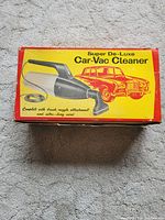 Original closed box of yellow and red color labeled 'Super De-Luxe Car-Vac Cleaner' with vintage car graphic
