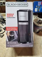 Front view of the Black & Decker Single Serve Coffeemaker box showing brand, model type, and travel mug included.