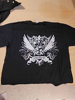 Black large size t-shirt laid flat showing front white graphic with skull, guitar, wings, decorative swirls and 'Dean Established 1977' text.