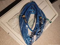 Full view of coiled blue marine hose inside transparent packaging on a white surface.