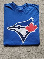Blue Jays blue T-shirt folded with large logo of blue jay head and red maple leaf on front.