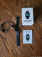 ID207 Smart Watch with USB charging cable, manual, and box on wooden floor