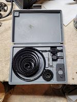 Opened gray plastic case showing multiple black metal hole saw blades of varying sizes arranged inside.