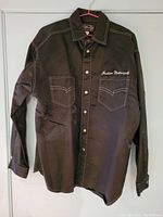 Front view of black long sleeve button-up shirt with Indian Motorcycle embroidery on left chest pocket, white stitching, two chest pockets with buttons, collar, and button-down front.