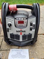 Front view of the Schumacher XPF2260 jump starter showing the digital display, power switches, dial, outlets, and handle with a hanging tag.