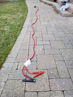Full length of the red jumper cable with metal clamps, stretched out on a driveway surface.