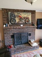 Wide view of 3D metal motorcycle wall art mounted above fireplace on brick wall.