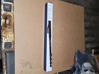 Photo showing the box of the Insignia monopod standing upright on a brown surface with a rusty metal edge nearby.