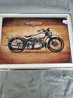 Metal sign showing a vintage Harley-Davidson motorcycle on a wood plank background with some paint chipped on the corner.