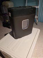Front and side view of black paper shredder with basket showing compact size and window on basket.